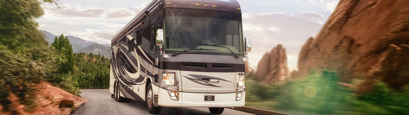 A white and gray RV travels down a road with mountains and canyons.