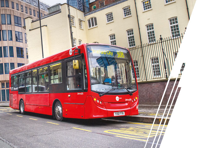 A red, white and blue bus travels under an overpass.
