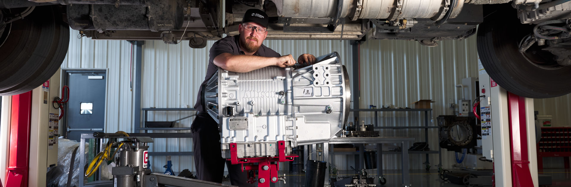An Allison technician stands below a vehicle leaning against an Allison transmission.